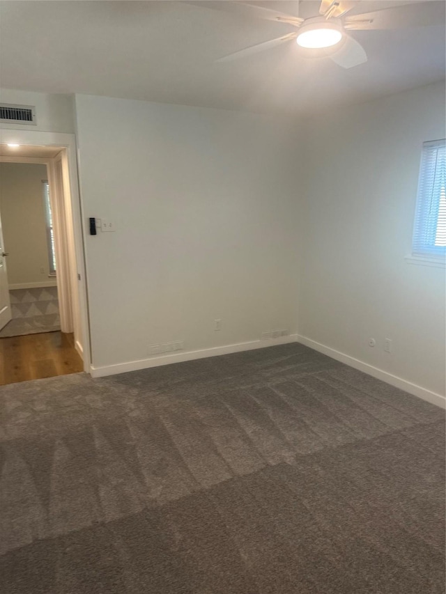empty room with baseboards, dark colored carpet, a ceiling fan, and visible vents