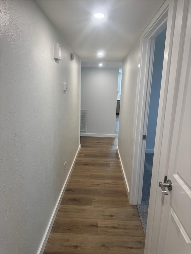 corridor with dark wood-type flooring, visible vents, baseboards, and recessed lighting