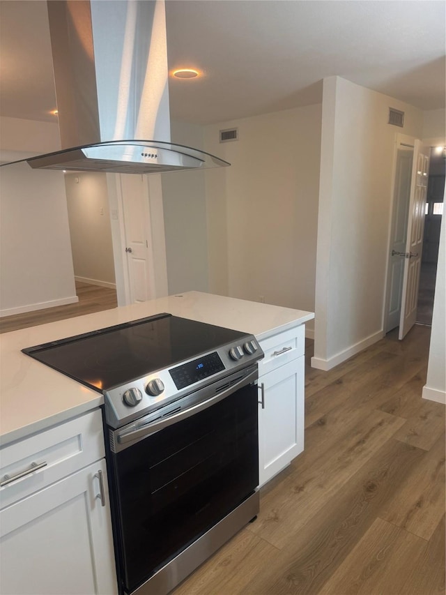 kitchen featuring light wood finished floors, stainless steel electric range, island range hood, and visible vents