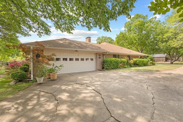 view of front of house featuring an attached garage, driveway, a chimney, and brick siding