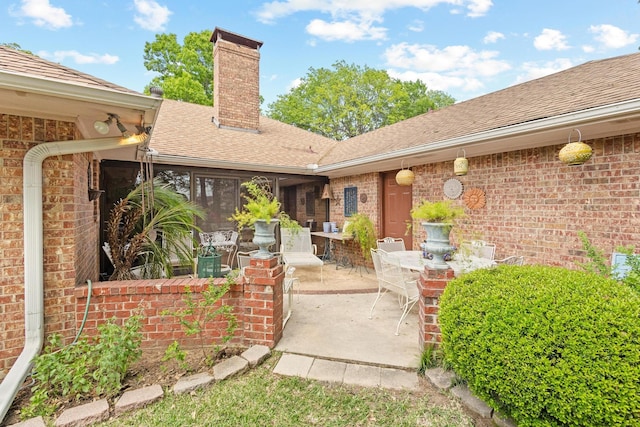 property entrance featuring a patio area, a chimney, outdoor dining space, a shingled roof, and brick siding