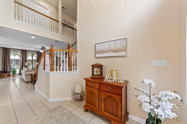 interior space featuring stairway, light tile patterned flooring, a towering ceiling, baseboards, and visible vents