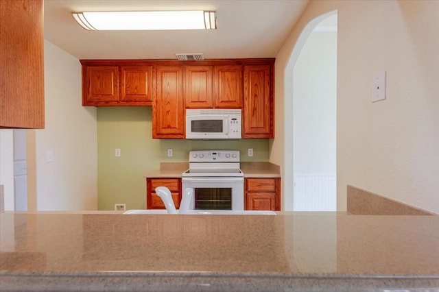 kitchen featuring brown cabinetry, arched walkways, visible vents, and white appliances