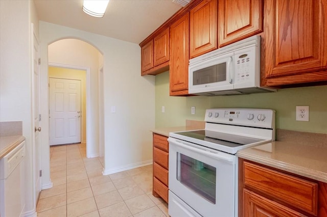 kitchen featuring arched walkways, white appliances, brown cabinets, light countertops, and light tile patterned floors