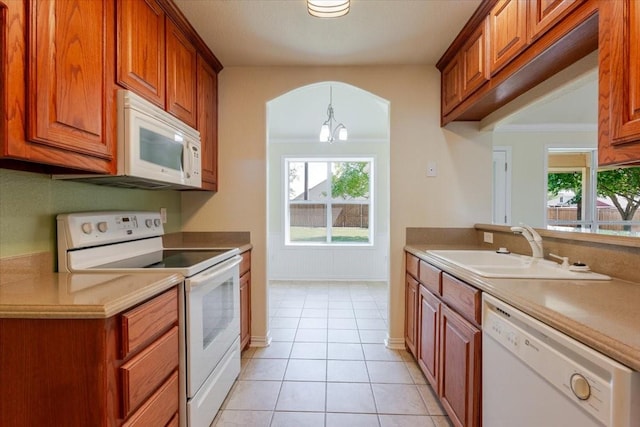 kitchen with brown cabinets, light tile patterned floors, a sink, and white appliances
