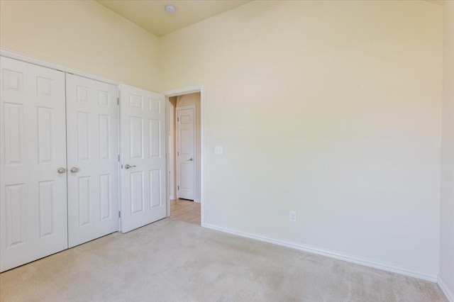 unfurnished bedroom with light colored carpet, baseboards, and a closet