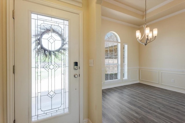 foyer featuring dark wood-style floors, wainscoting, a notable chandelier, a decorative wall, and ornamental molding