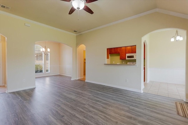 unfurnished living room featuring arched walkways, visible vents, ceiling fan with notable chandelier, wood finished floors, and crown molding
