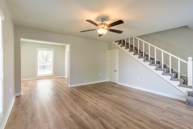 unfurnished living room with stairway, ceiling fan, baseboards, and wood finished floors