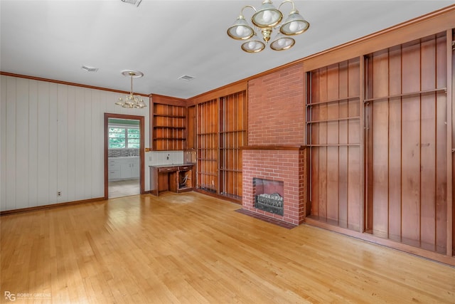 unfurnished living room featuring visible vents, a brick fireplace, light wood-style floors, and a chandelier