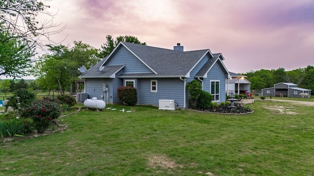 rear view of property featuring a chimney, roof with shingles, and a yard