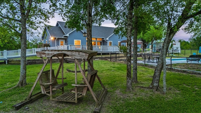 back of property at dusk with fence, a wooden deck, roof with shingles, and a yard