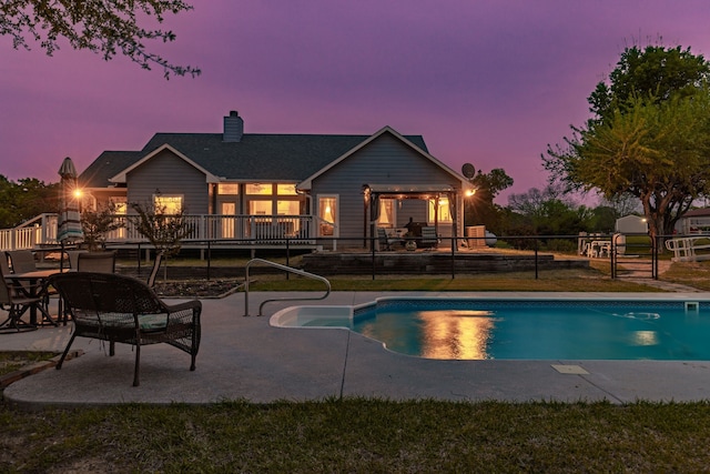 pool at dusk with a wooden deck, a patio area, an outdoor pool, and fence
