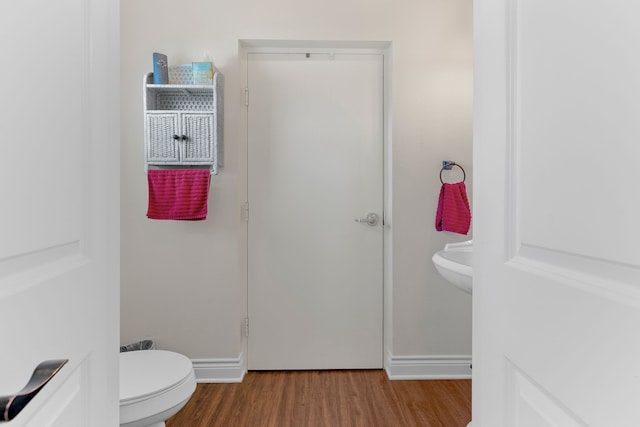 bathroom with baseboards, wood finished floors, and toilet
