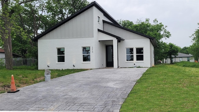 contemporary home with fence, board and batten siding, a front yard, and brick siding