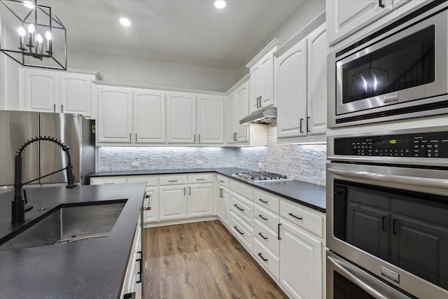 kitchen with white cabinets, stainless steel appliances, dark countertops, and a sink