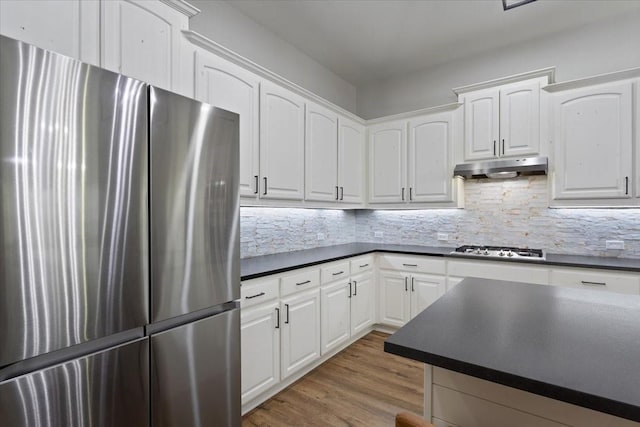 kitchen with dark countertops, white cabinetry, under cabinet range hood, backsplash, and stainless steel appliances