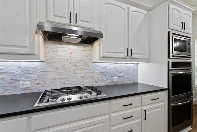 kitchen featuring dark countertops, appliances with stainless steel finishes, white cabinetry, decorative backsplash, and under cabinet range hood