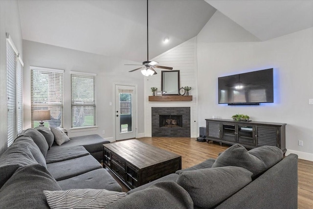 living room featuring wood finished floors, a fireplace, baseboards, ceiling fan, and high vaulted ceiling