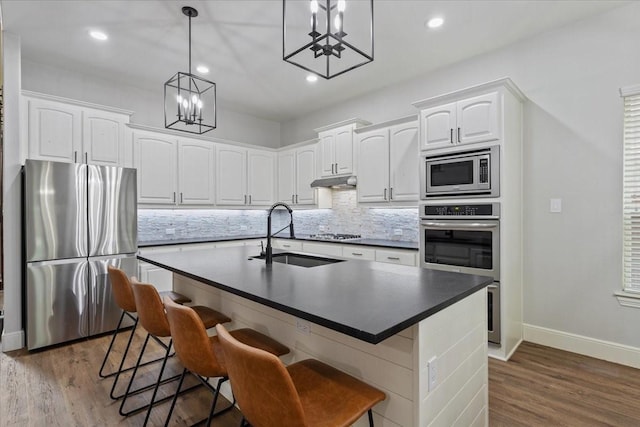 kitchen with dark countertops, a sink, baseboards, a notable chandelier, and stainless steel appliances