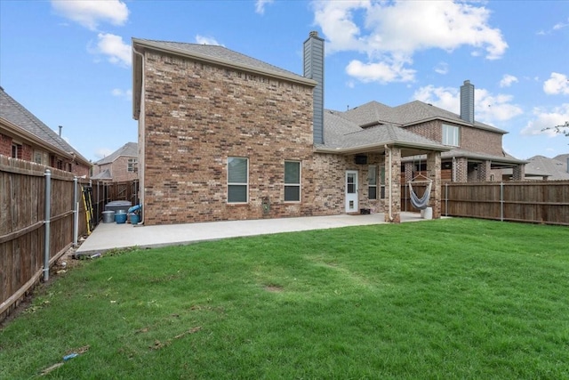 rear view of property with brick siding, a fenced backyard, a patio area, and a yard