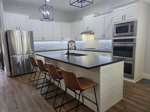 kitchen with decorative backsplash, dark countertops, a sink, stainless steel appliances, and dark wood-type flooring
