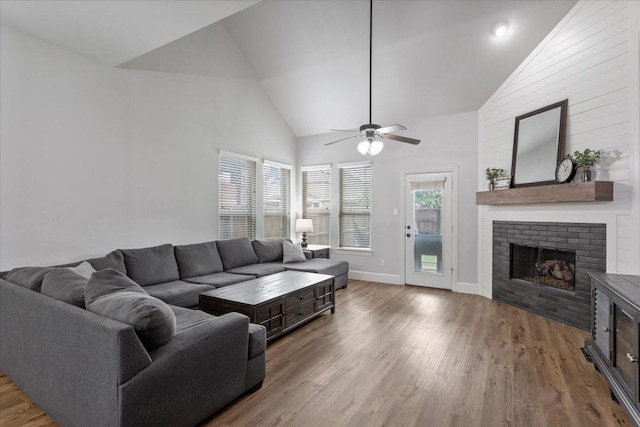 living area with a ceiling fan, a brick fireplace, wood finished floors, high vaulted ceiling, and baseboards