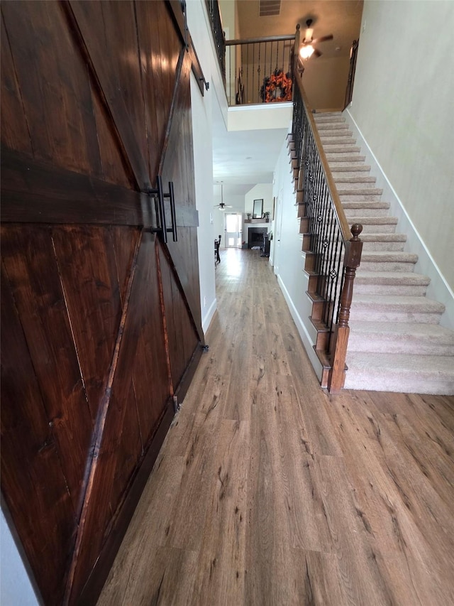 stairs featuring visible vents, a barn door, wood finished floors, baseboards, and a high ceiling