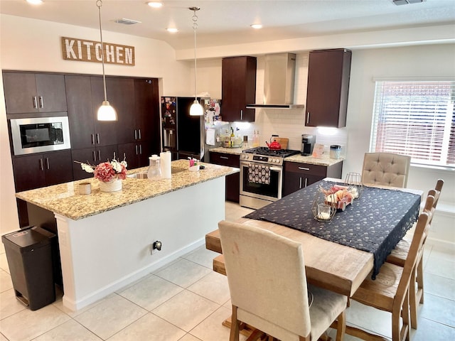 kitchen with built in microwave, stainless steel range with gas stovetop, wall chimney range hood, visible vents, and black fridge