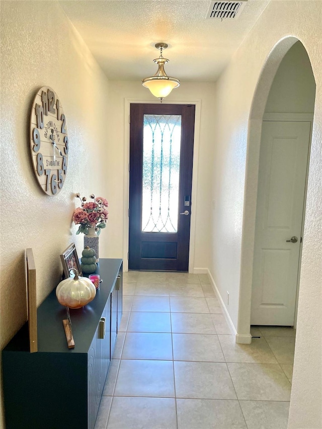 entryway featuring a textured wall, visible vents, arched walkways, and light tile patterned floors