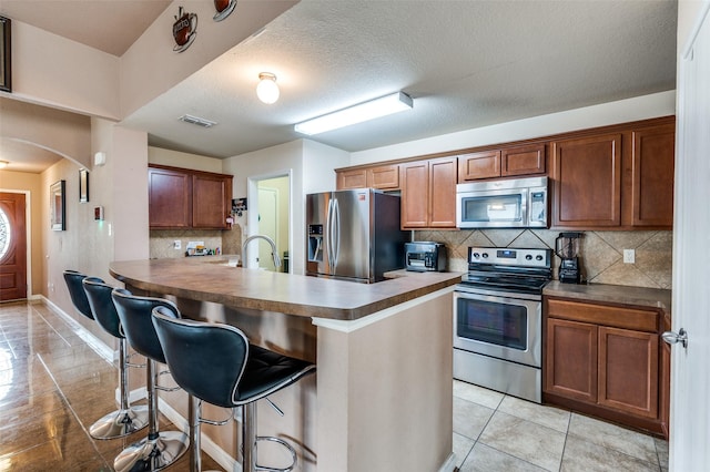 kitchen featuring a kitchen breakfast bar, stainless steel appliances, visible vents, light tile patterned floors, and arched walkways