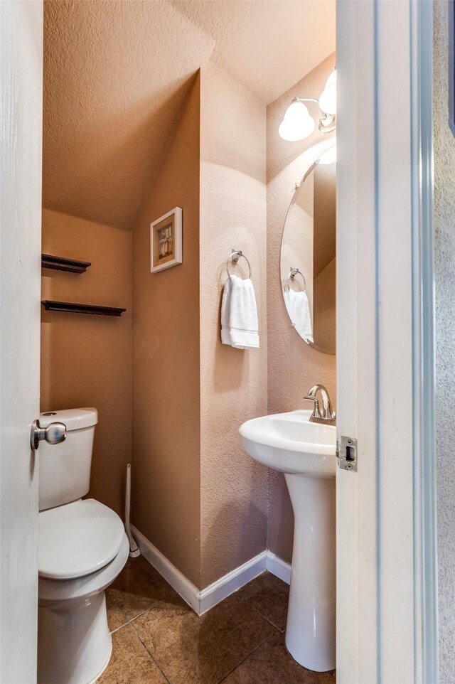 bathroom featuring vaulted ceiling, a textured ceiling, baseboards, toilet, and tile patterned flooring