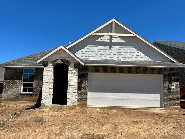 view of front of property featuring brick siding, stone siding, and a garage