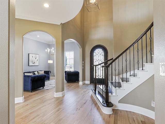 foyer with stairway, a high ceiling, wood finished floors, arched walkways, and baseboards