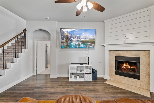 living area featuring baseboards, wood finished floors, stairs, ceiling fan, and a tile fireplace