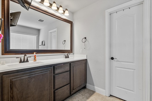 bathroom featuring a sink, double vanity, baseboards, visible vents, and tile patterned flooring