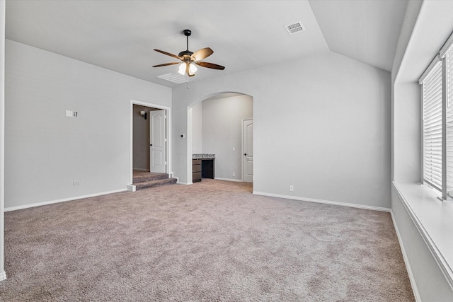 empty room with carpet flooring, arched walkways, vaulted ceiling, visible vents, and ceiling fan