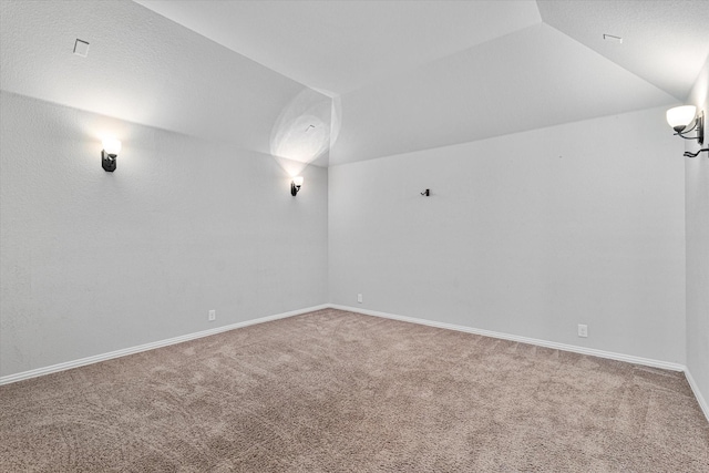 carpeted empty room featuring vaulted ceiling and baseboards