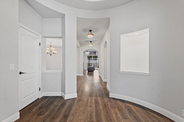 corridor featuring arched walkways, wood finished floors, baseboards, and an inviting chandelier