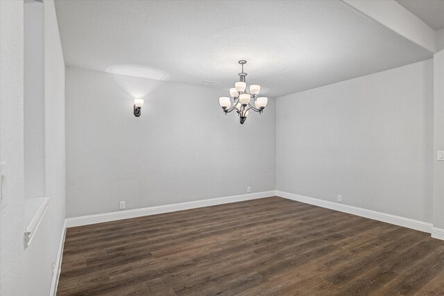 spare room with a chandelier, baseboards, and dark wood-style flooring