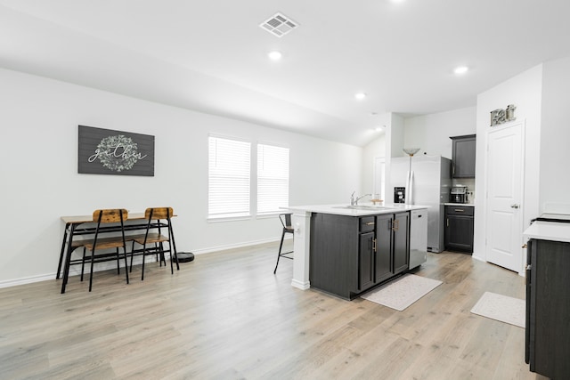 kitchen featuring a kitchen breakfast bar, a kitchen island with sink, visible vents, and light countertops
