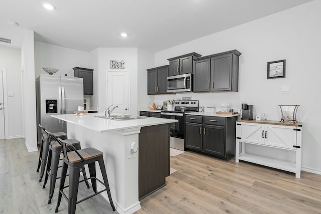kitchen featuring stainless steel appliances, light countertops, a sink, light wood-style floors, and a breakfast bar