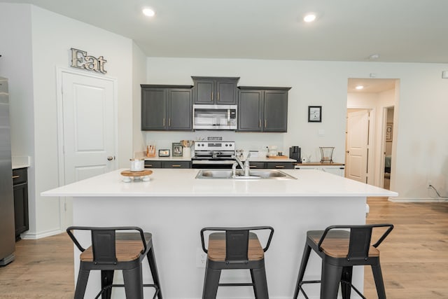 kitchen with appliances with stainless steel finishes, a sink, light wood-style floors, and a breakfast bar area