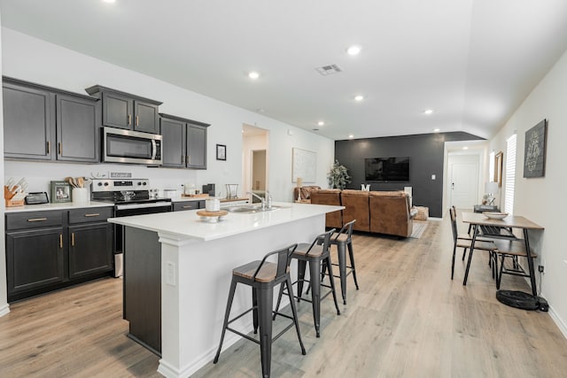 kitchen with a kitchen island with sink, light countertops, light wood-type flooring, a breakfast bar, and appliances with stainless steel finishes