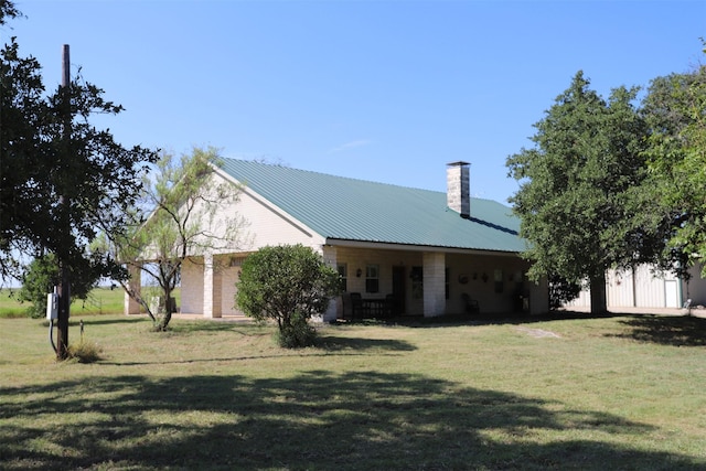 rear view of house with a chimney, a yard, and metal roof