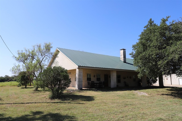 back of house with stone siding, a lawn, a chimney, and metal roof
