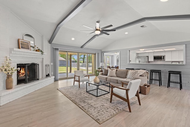 living area featuring light wood-style floors, ceiling fan, lofted ceiling, a brick fireplace, and visible vents