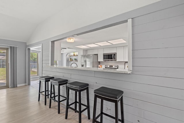 kitchen featuring vaulted ceiling, white cabinetry, a kitchen breakfast bar, and stainless steel appliances