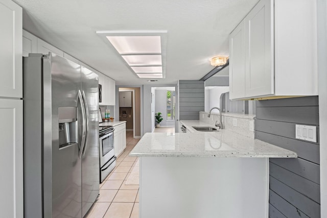 kitchen with white cabinets, stainless steel appliances, light tile patterned floors, a sink, and a peninsula