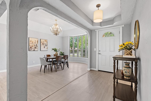 entrance foyer with baseboards, light wood-style floors, a notable chandelier, and a raised ceiling